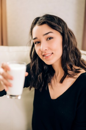 Charming smiling brunette girl with french manicure holding glass of milk. Health care, diet, vitamins, wellness, healthy drink. Close up.の写真素材