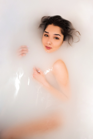 Beautiful young sexy girl with dark hair and natural makeup, takes bath with milk, beauty cosmetic salon and spa for woman.の写真素材