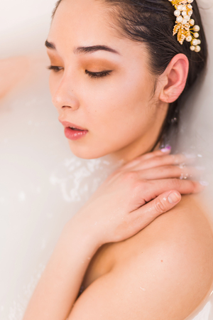 Closeup portrait of a young woman relaxing in the milk water. Girl profile with closed eyes in bathの写真素材
