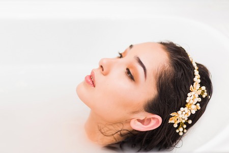 Close up woman face profile with decoration on the head lying in a milk bathの写真素材