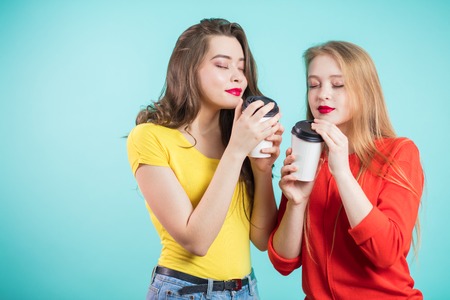 Two smiling students girls drinking morning coffee, inhale the aroma of coffee. Pleasure,...