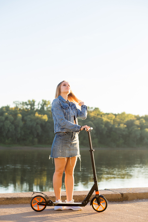 Beautiful blonde woman in jeans with scooter on the waterfront.の写真素材