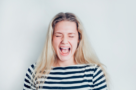 A portrait of very frustrated and angry woman on white background. Beautiful blonde girl screams. Expressive facial expressions, negative emotionsの写真素材
