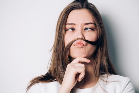 Fun prank joy entertainment concept. Silly lady playing with hairs. Young playful girl making mock moustache using her own hair.の写真素材
