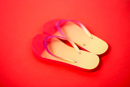 Yellow pink flip flops on red background. Flat lay, horizontal shot, close up. Summer, vacation, beach, shoes conceptの写真素材