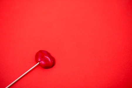 Sweet red lollipop in the shape of lips. Colour lollipop on coral background with copy space. Top view, close up. Valentine's day, sweets, candy, minimal concept.の写真素材