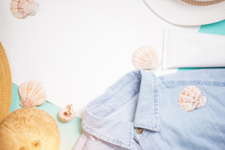Top view of female holiday clothing and summer accessories. Blue denim shirt, sun hat, sunblock, coconut, seashells on light blue background with blank white paper.の写真素材