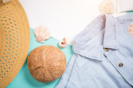 Composition from womans blue denim shirt, beach straw hat, seashells, coconut and sunscreen. Top view, selected focus. Fashion blogger, summer accessories and holiday concept.の写真素材