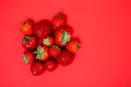 Flat lay photo of ripe red fresh juicy strawberries with green leaves on coral background with copy space for text. Berry, garden, dessert, summer, food concept.の写真素材