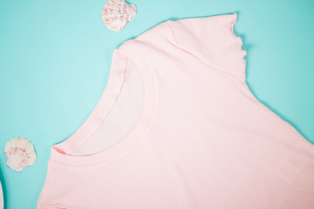 Pale pink cotton t shirt and seashells on mint background. Women's clothing, store, shop, summer, spring collection, vacation, holiday concept. Flat lay.の写真素材