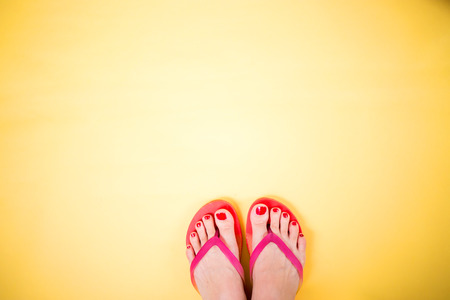 Woman's legs with red pedicure wearing pink flip flops on yellow background with copy space. Summer, vacation, travel, beach concept.の写真素材
