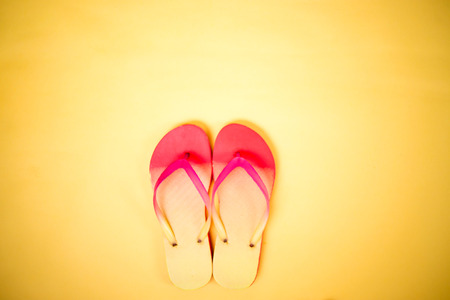 Coral pink flip flops on yellow background with copy space. Flat lay, horizontal shot. Summertime, vacation, beach, shoes concept.の写真素材