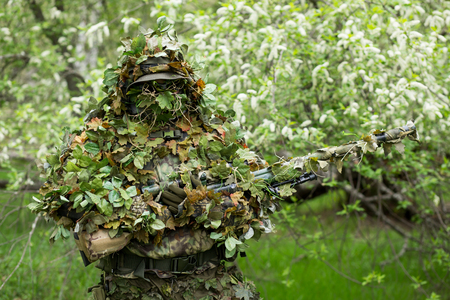 Closeup portrait of a military sniper men in camouflage green army clothes with a gun on his hand on the background of flowering treesの写真素材