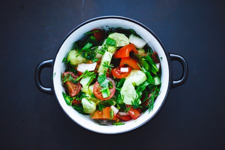 summer salad of fresh vegetables in a plate on a black background, tomatoes, cucumbers, dill, parsley, onion. Close up, top view.の写真素材