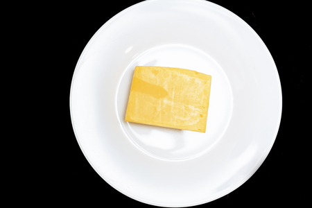 Closeup of a piece of cheese on a white plate on a black background. Natural dairy products, delicious food conceptの写真素材
