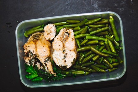 Healthy snack, food in a container. Baked red fish, pink salmon, salmon and green beans on black...