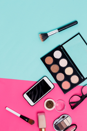 Flat lay of makeup products smartphone and women glasses blue and pink background, top view. Face concealer, nail Polish, brush, Foundation, eye shadow and glitter. Close up, top viewの写真素材