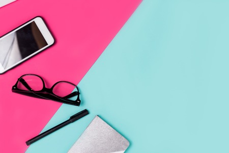 Flat lay traveler and office accessories on a colored background with copy space. Notebook, smartphone, glasses, pen, lipstick, lip gloss on the table at the girlの写真素材