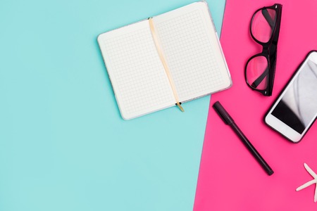 Home office desk with Notepad, smartphone, glasses, pen on a colorful background, top view. Close up