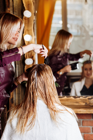 Close up shot of hands of hairdresser with brush applying mask or conditioner to hair of her client in beauty hair salon. Spa, care, hair health, problems with hair.の写真素材