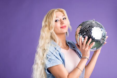 Studio portrait of beautiful stylish lovely blonde long haired woman posing with shining disco ball,...