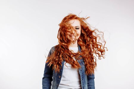 Attractive cheerful redhead girl with flying curly hair smiling over white background. Copy space.
