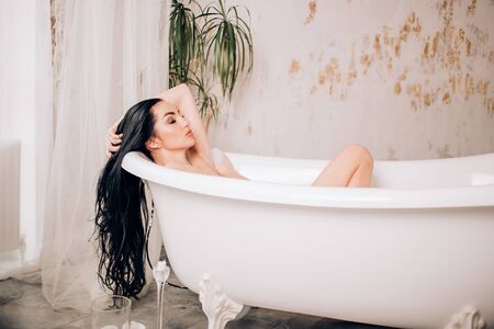 Attractive young naked woman with healthy white skin, perfect skin, long black healthy hair, with closed eyes chilling in spa salon, taking bath with pleasure expression in modern bathroom.の写真素材