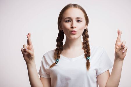 Cheerful happy young woman wearing glasses and a t-shirt makes a funny grimace, crosses her fingers on white background. Human emotions, facial expression conceptの写真素材
