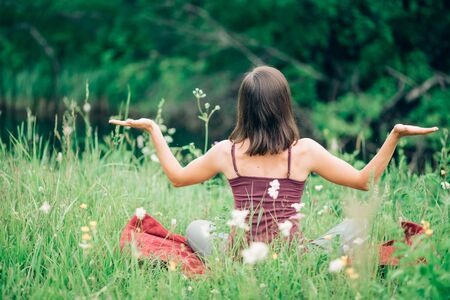 Young woman sitting back with her hands open in nature in the summerの写真素材