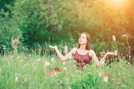 Young woman with open hands sitting in a clearing, doing yogaの写真素材