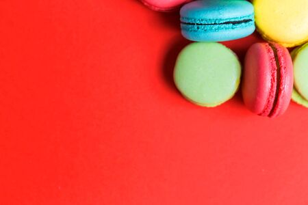 Closeup of red background for copy space with colorful macaroons in the corner. Sweet green, yellow, coral, blue French pastriesの写真素材