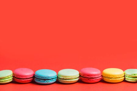 Bright red background for text with colorful yellow, green, blue, pink macaroons. Copy space for pastry chef, cafe, bakeryの写真素材