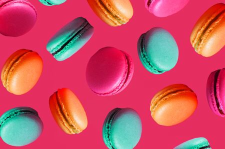 Different types of macaroons in motion falling on a pink background. Turquoise, orange sweet French...