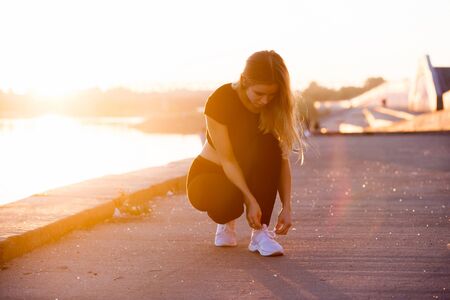 Picture of young attractive fitness woman on sunset background. Young blonde girl tying Shoe laces while runningの写真素材