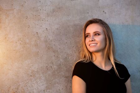 Horizontal portrait of beautiful smiling blonde woman on outdoor wall background with copyspace. The...
