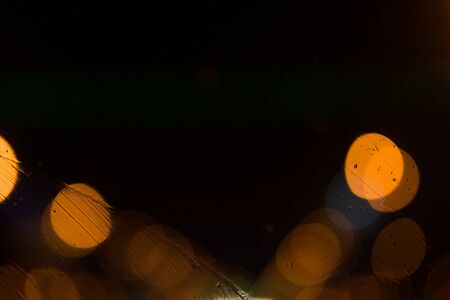 Dark abstract background with bright orange and yellow bokeh with raindrops on the street at night...