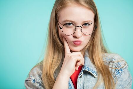 Pretty girl with glasses is determined and thinking looks at the camera on blue background. piercing lookの写真素材