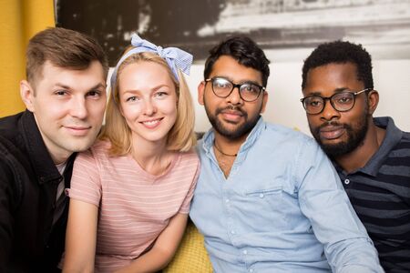Closeup portrait of four multi ethnic friends in home interior. Students sitting on couch smiling taking selfie together. People, friendship concept.の写真素材
