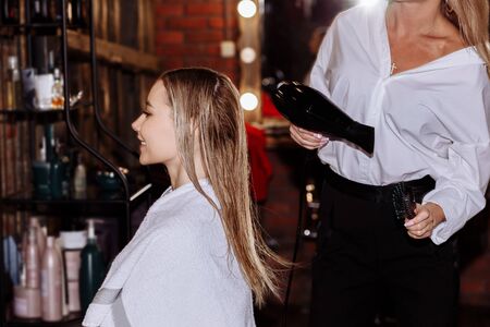 Cute beautiful hairdresser making hairstyle to young woman after haircut in beauty salon. Hair care, beauty concept.の写真素材