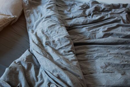 A gray cotton sheet and blankets with pillows on the bedの写真素材