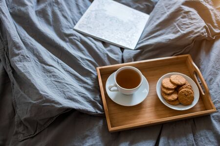 Breakfast of tea and biscuits with a magazine in a grey bed in the morning