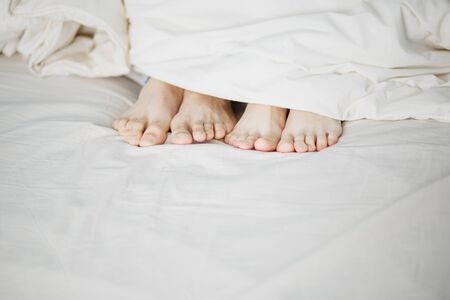 the legs of two lovers men and women protrude protrude under the white soft fluffy clean blanket on...