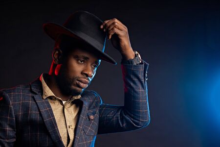 Handsome serious business African American man in hat on black background with blue and red lights...