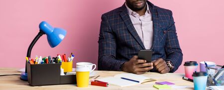 Stylish handsome afro american businessman sitting at desk in office, holding smartphone, checking...