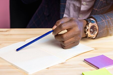 Close up cropped shot of dark skinned male hand holding pen. Businessman wearing suit, stylish wrist...