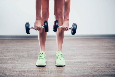 black large dumbbell in the hands of the girls legs in green shoes, and bent down to the floor, closeup, white backgroundの写真素材