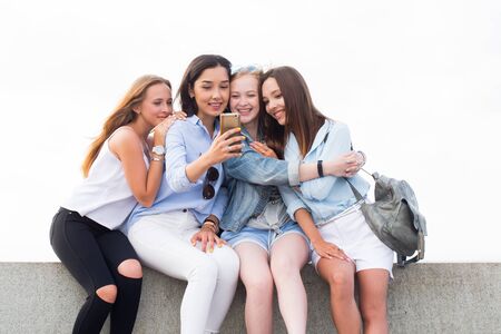 Happy charming student girl sit, using smartphone and smiling in the Park on the background of skyの写真素材