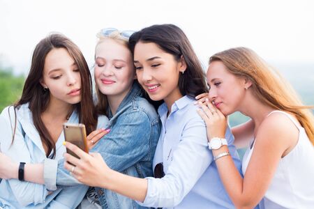 Close up of four beautiful young female students doing selfies and smiling on the background of...