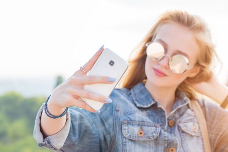 A woman in sunglasses takes a selfie on the background of nature. Smartphone in focusの写真素材