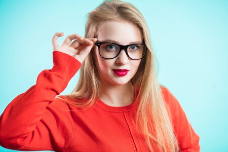 A young girl shows the fashionable glasses. Beautiful woman with red lips and dress on blue background. ophthalmologyの写真素材